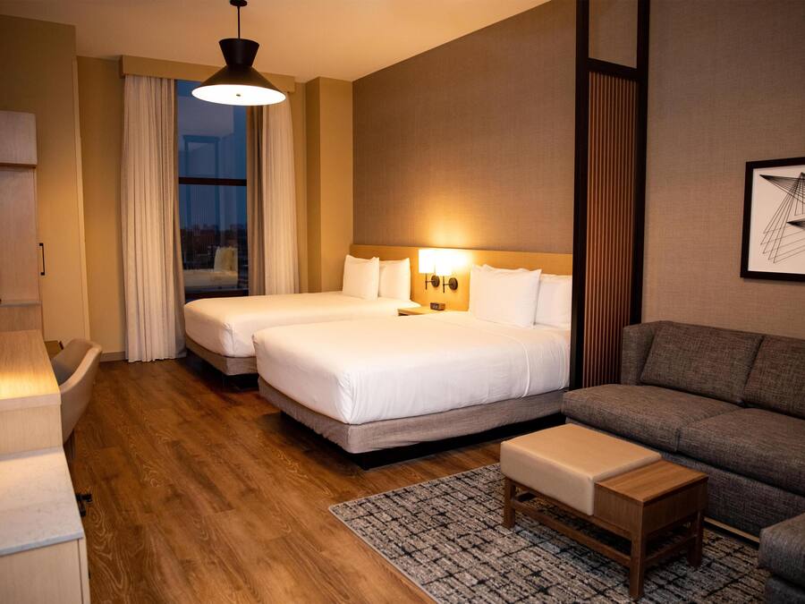 A hotel room with two beds, a sofa, a desk, and a large window with curtains.