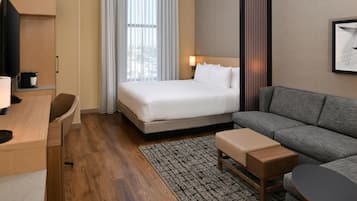 A hotel room with a bed, a sofa, a desk, a TV, and a window with curtains.