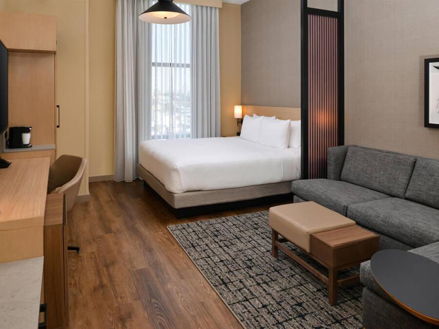 A hotel room with a bed, a sofa, a desk, a TV, and a window with curtains.