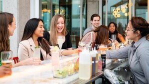 A group of people seated at a table with drinks and a salad, in a modern indoor setting with large windows and a bar area. - Hyatt Place Chicago/Wicker Park (Chicago)
