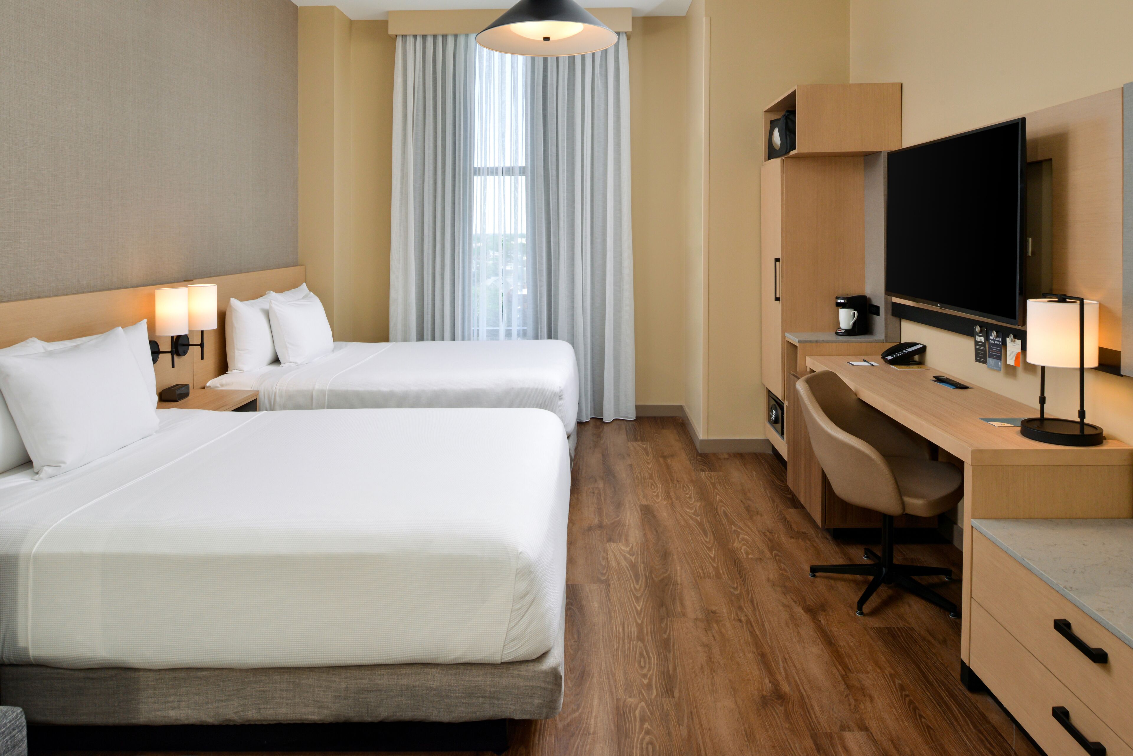Habitación de hotel con dos camas, un escritorio, una silla, un televisor y una ventana con cortinas.