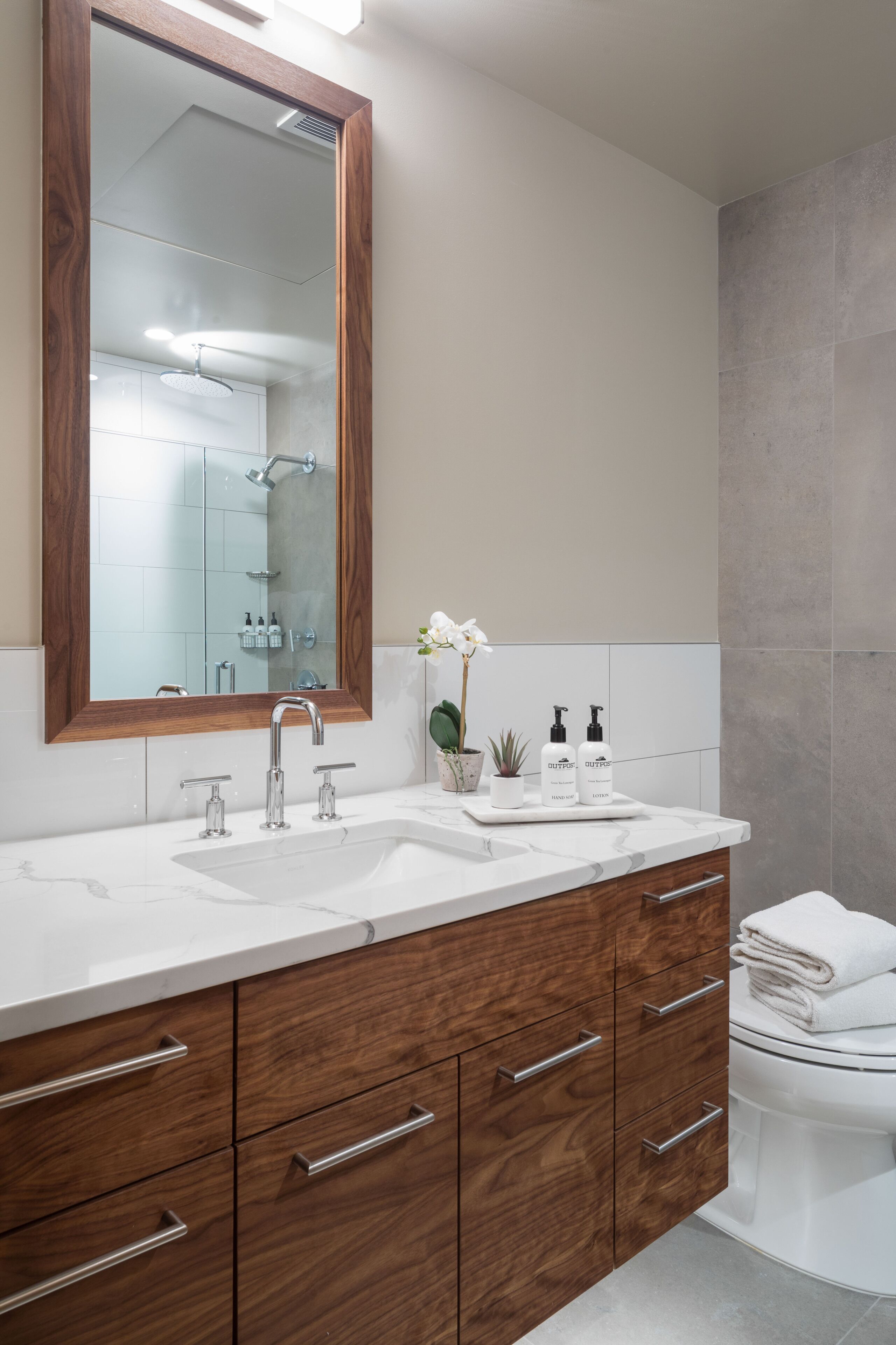 A modern bathroom with a wooden vanity, a large mirror, a white sink, and a toilet.