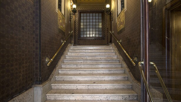 A marble staircase with ornate wall designs and a glass door at the top.