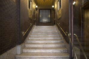 A marble staircase with ornate wall designs and a glass door at the top. - Coppedè Flat Two, Palazzo degli Ambasciatori (Roma)