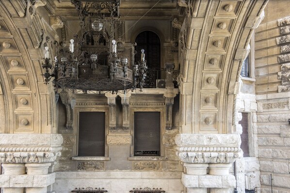 An ornate building facade with intricate carvings, a large chandelier, and closed shutters. - Coppedè Flat Two, Palazzo degli Ambasciatori (Roma)
