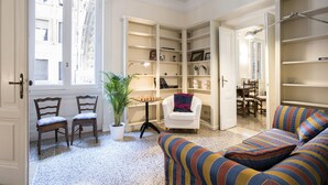A room with a chess table, a potted plant, a striped sofa, and a bookshelf.