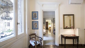 A hallway with a wooden chair, a desk with a lamp, and two framed pictures on the wall.