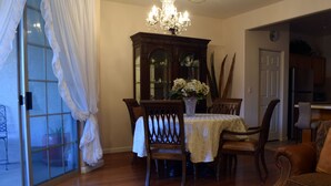 Un coin repas avec une table dressée pour quatre personnes, entourée de chaises en bois, d’un lustre et d’un grand miroir placé au-dessus de la table.