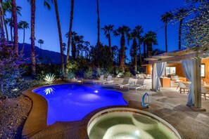 A swimming pool with a curved edge, surrounded by palm trees and a mountain in the background.