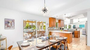 A modern kitchen with a central island, dining area with chairs, and a view to the outside. - Modern Loma Vista – Private Pool & Spa Retreat (Palm Springs)