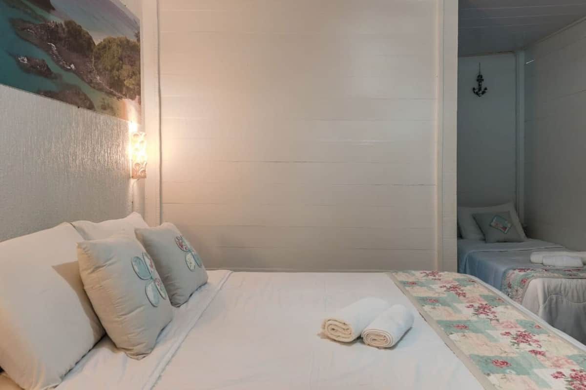 A hotel room with a bed, two bedside tables, a nightstand, a wall-mounted lamp, and a painting.