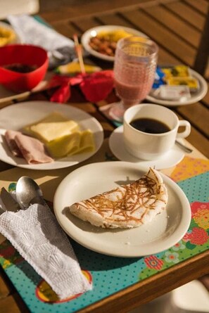 A table with a plate of food, a glass of beverage, and a napkin. - Pousada Carmo (Fernando de Noronha)