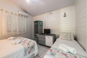 A bedroom with two beds, a desk, a chair, an air conditioning unit, a television, and a wardrobe. - Pousada Carmo (Fernando de Noronha)