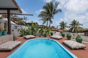 A swimming pool with lounge chairs, surrounded by potted plants and palm trees. - Pousada Carmo (Fernando de Noronha)