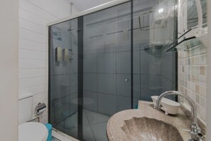 A bathroom with a glass-enclosed shower, a sink with a granite countertop, and a toilet. - Pousada Carmo (Fernando de Noronha)