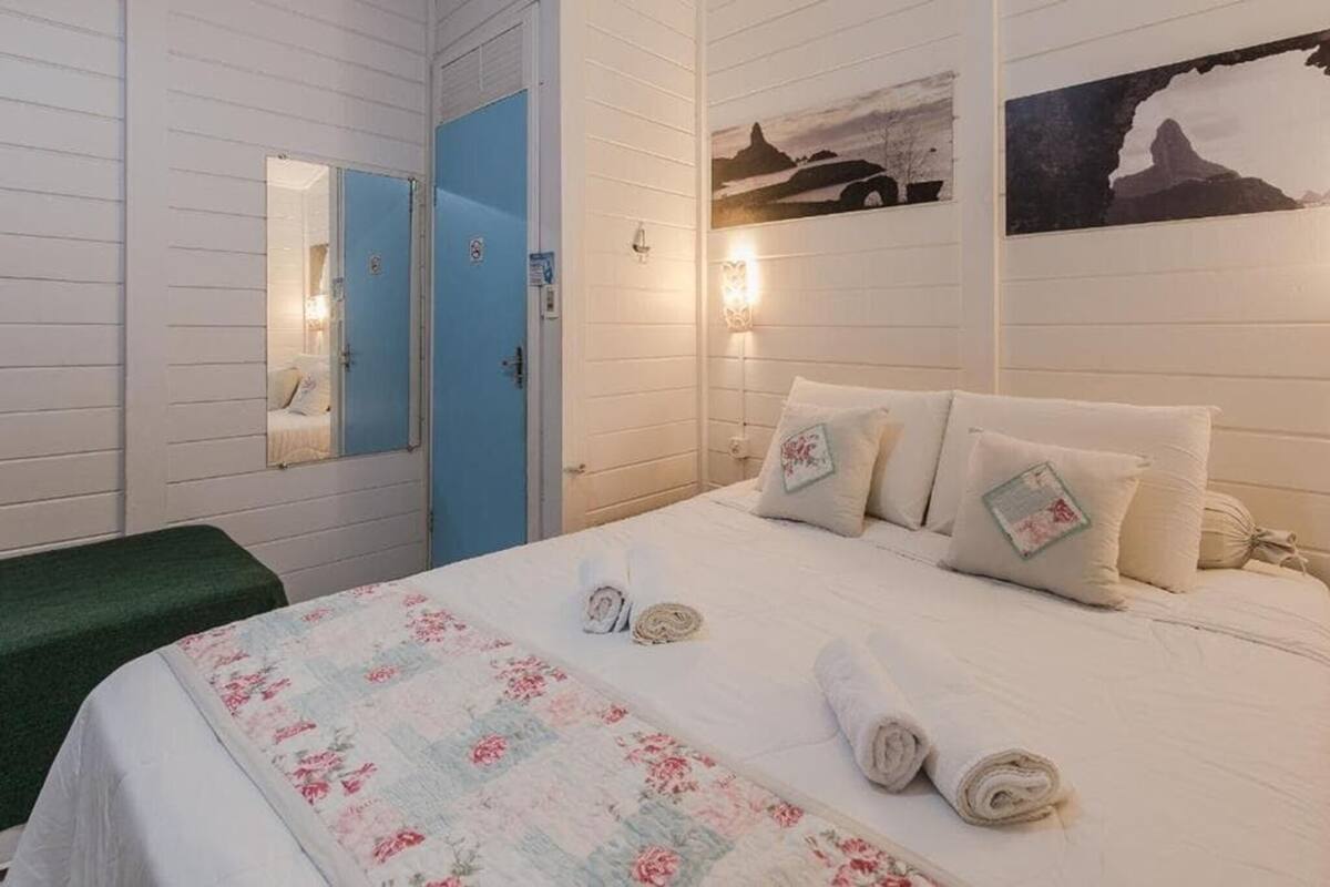 A hotel room with a bed, a green bench, a blue door, and wall-mounted artwork.