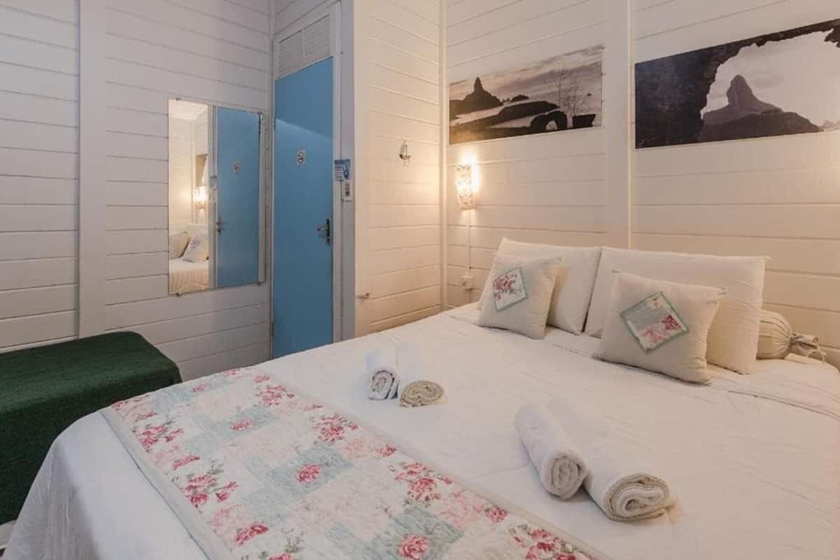 A hotel room with a bed, a green bench, a blue door, and wall-mounted artwork.