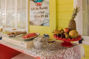 Ontbijtbuffet met een bord waarop de openingstijden van Café da Manhã staan vermeld, een presentatie van fruit en een warme ontbijtsectie.