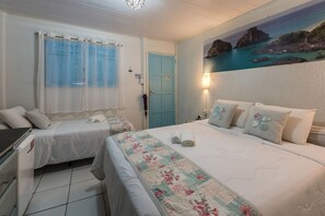 A bedroom with two beds, a painting of a coastal scene, a blue door, and a white dresser. - Pousada Carmo (Fernando de Noronha)