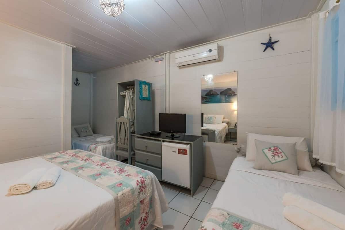 A room with two beds, a desk with a computer, an air conditioner, and a mirror reflecting a scenic view.