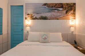 A bedroom with a bed, a blue door, and a wall-mounted painting of a beach scene. - Pousada Carmo (Fernando de Noronha)