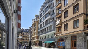 Una calle con edificios de varios pisos, un restaurante y una tienda con toldo azul.