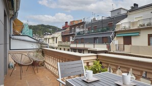 Una terraza con una mesa, sillas, una taza blanca y una planta en maceta.