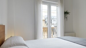 Un dormitorio con un ventanal grande, una cama, un radiador y una planta.