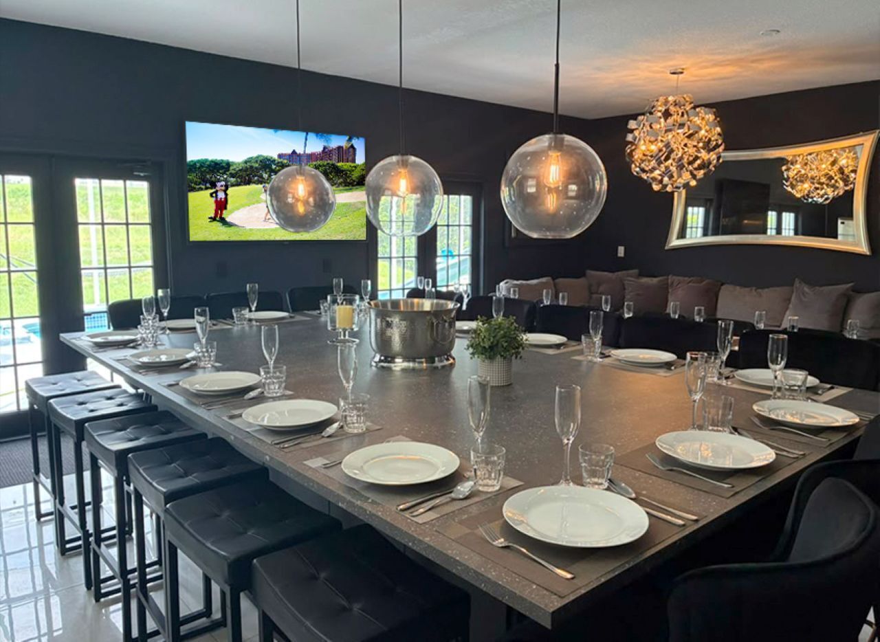 A dining area with a long table set for a meal, a television mounted on the wall, and a large mirror.