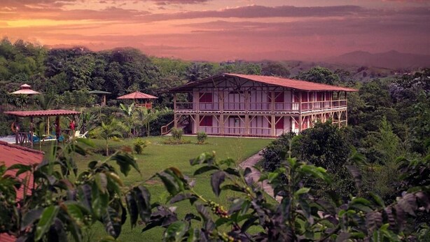 A large, two-story building with a red roof and white walls, surrounded by lush greenery and hills in the background. - Socialtel Filandia (Filandia)