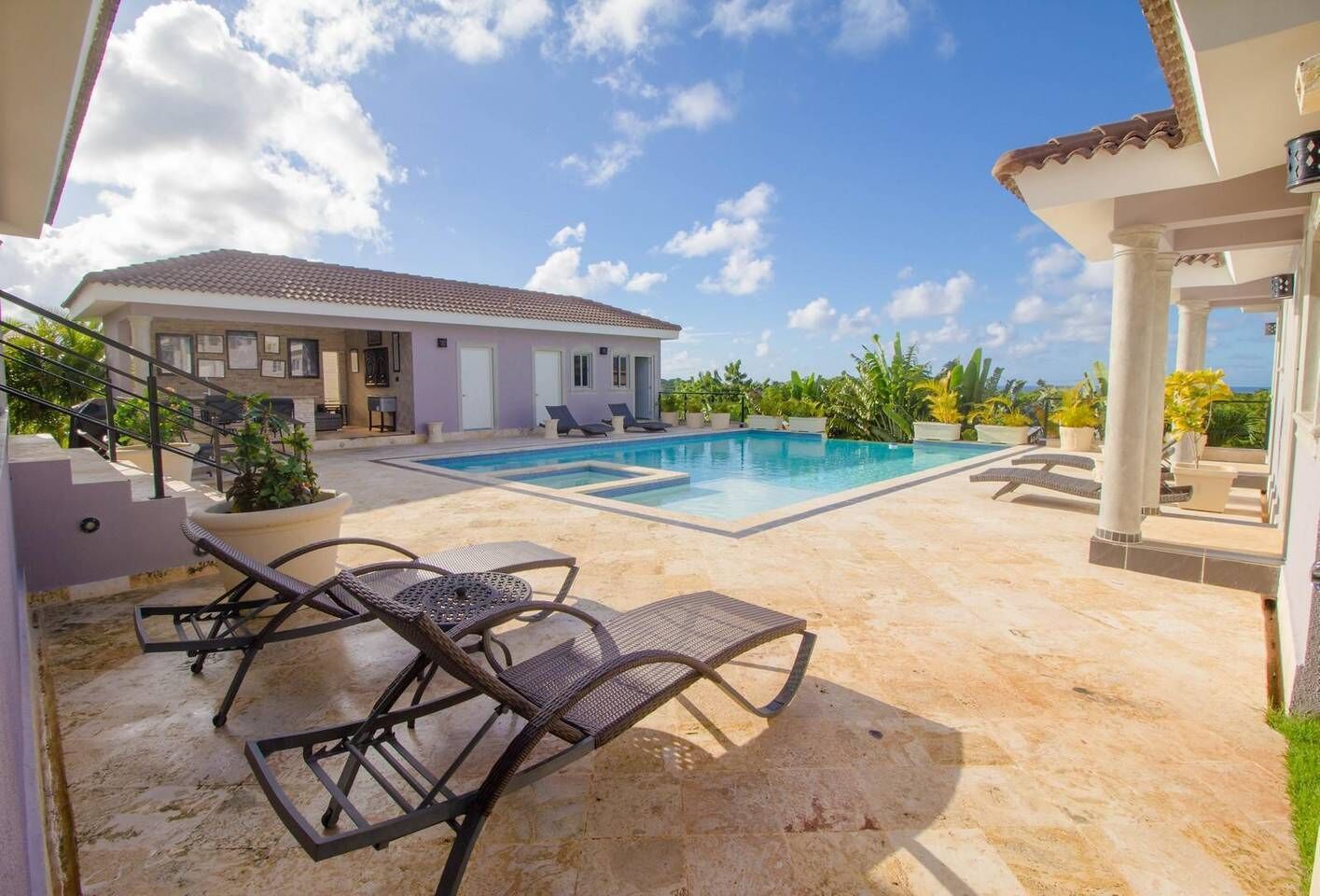 A pool area with lounge chairs, a staircase, and a building with a tiled roof.