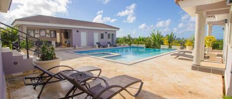 A pool area with lounge chairs, a staircase, and a building with a tiled roof.