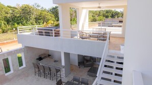 Une terrasse extérieure moderne comprenant un espace repas, un barbecue et une vue sur la végétation environnante.