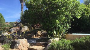 A garden with large rocks, a wooden bridge, and various plants. - CAEDA VILLA - PRIVATE SWIMMING POOL - SAINT CYPRIEN (SAINTE-LUCIE DE PORTO-VECCHIO)