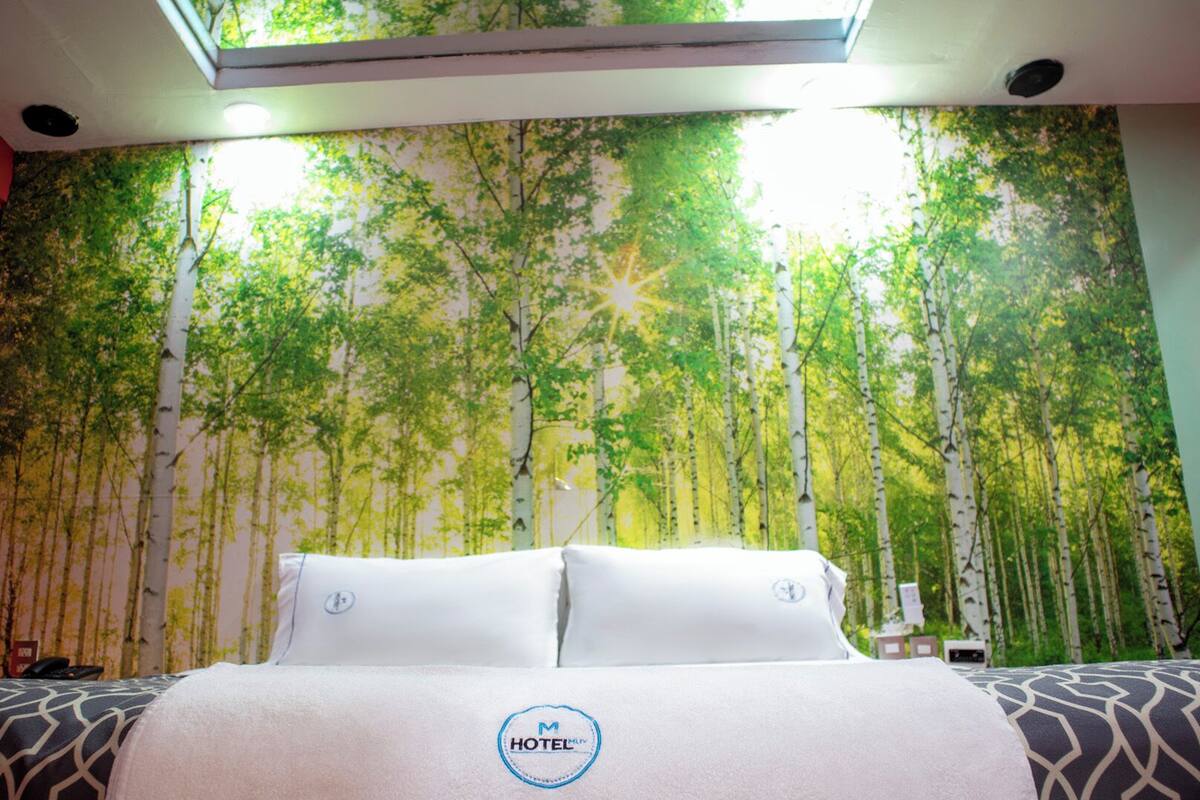 A hotel room with a bed, a desk, and a wall mural of a forest.