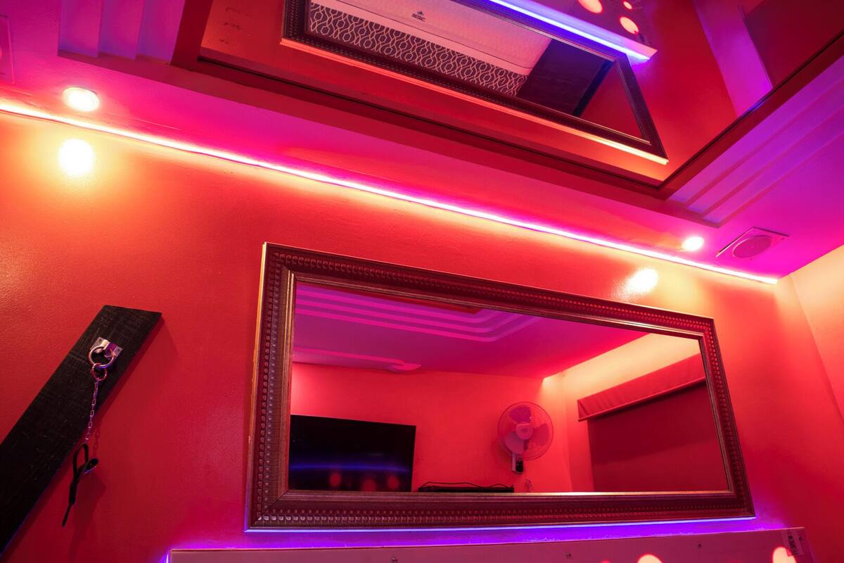 A bathroom with a large mirror, red walls, and purple lighting.