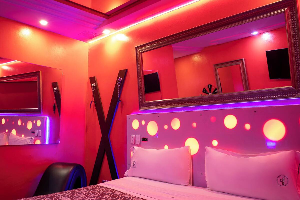 A hotel room with a bed, a large mirror, and a wall with circular light fixtures.