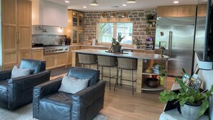 A modern kitchen with stone walls, wooden cabinets, a stainless steel refrigerator, and a bar area with bar stools. - Stunning Home in Historic Franklin, TN

Walk to Downtown, pickleball, & coffee! (Franklin)