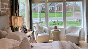 A bedroom with a large bed, two white chairs, a small table, a hanging lamp, and a view of a brick house through large windows. - Stunning Home in Historic Franklin, TN

Walk to Downtown, pickleball, & coffee! (Franklin)