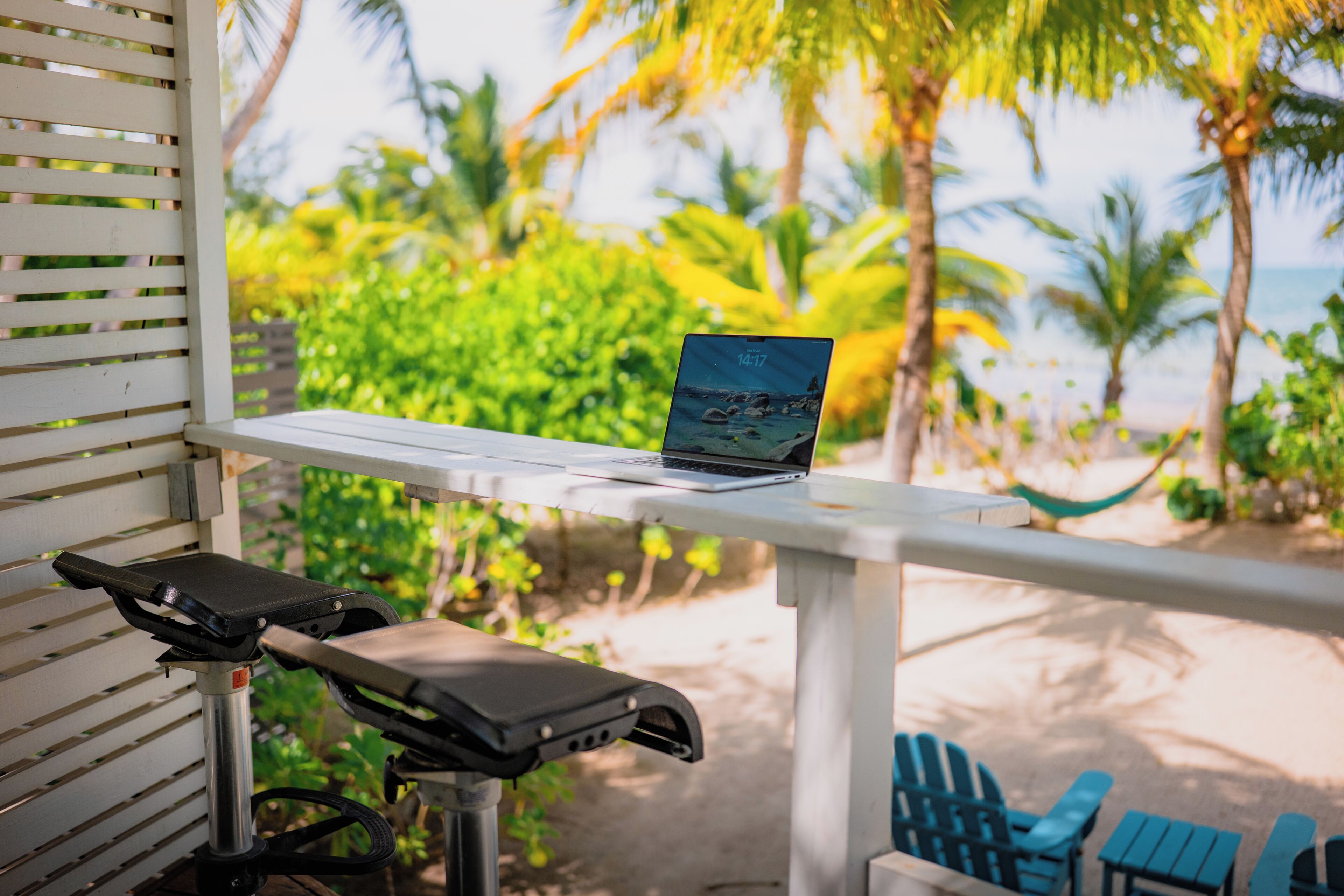 Un ordinateur portable est posé sur une table blanche, avec vue sur une plage et des palmiers.