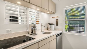 A modern kitchen with a built-in stove, a coffee maker, and a window with blinds. - OHANA WATA cabana, BEACHFRONT luxury, privacy, view & space IN the village ! (Placencia)
