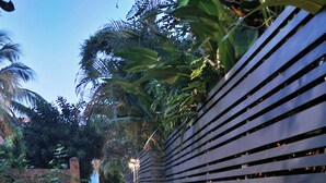 Uma passagem bordeada por uma cerca de madeira e vegetação exuberante, que leva a uma construção distante.