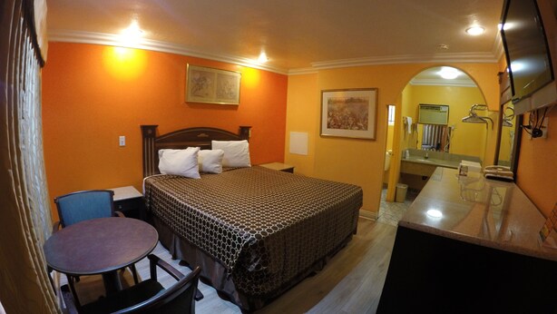 A hotel room with a bed, a desk, a chair, and a bathroom visible through an archway. - Calico Motel (Anaheim)