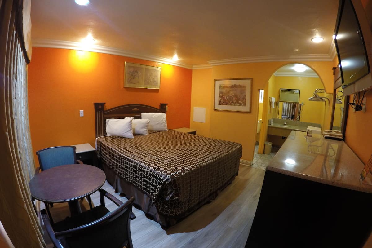 Camera d'albergo con un letto, una scrivania, una sedia e un bagno parzialmente visibile tramite un arco.