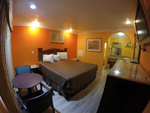 A hotel room with a bed, a desk, a chair, and a bathroom visible through an archway. - Calico Motel (Anaheim)