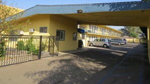 A yellow building with a covered entrance, a gated parking area, and a white car parked inside. - Calico Motel (Anaheim)