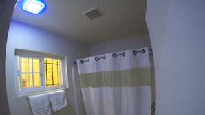 A bathroom with a toilet, a window with a curtain, and a shower curtain. - Calico Motel (Anaheim)