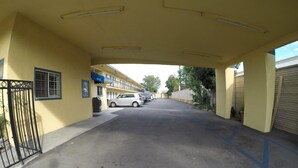 A parking area with a yellow building, a gated entrance, and a white car parked in the distance. - Calico Motel (Anaheim)
