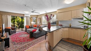 A modern kitchen with a central island, a dining area with a sofa and chairs, and a living room with a large rug and a TV. - Asiatic Suite at Nautilus Mooloolaba (Mooloolaba)