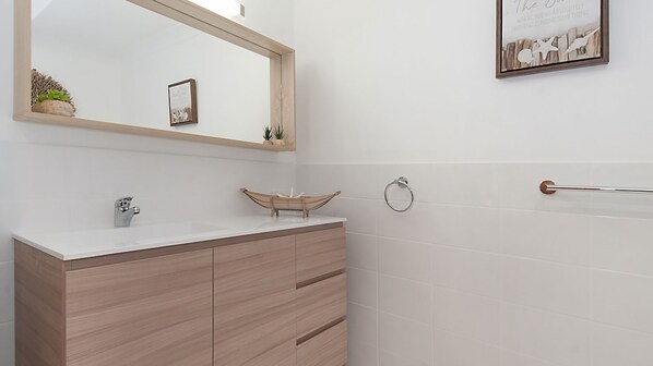 A bathroom with a wooden vanity, a large mirror, and a framed picture on the wall.